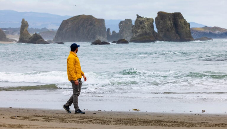 Person in a yellow jacket walking along the beach near the ocean