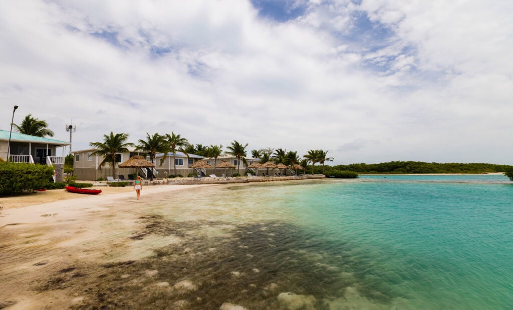 a woman walks on the beach in front of villas at shaka caye resort in belize