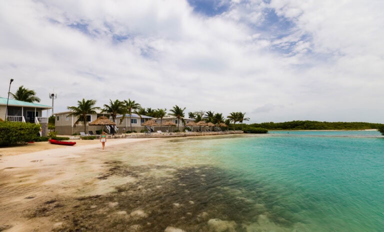 a woman walks on the beach in front of villas at shaka caye resort in belize