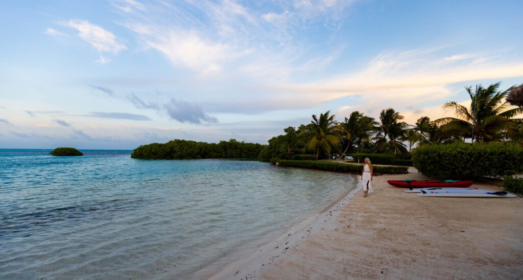 a woman in a white dress walks the beach at shaka caye resort