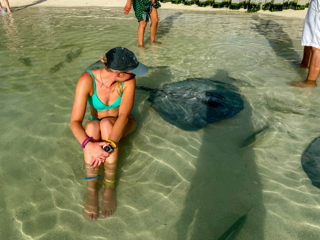 a woman sits in the water with a stingray nearby