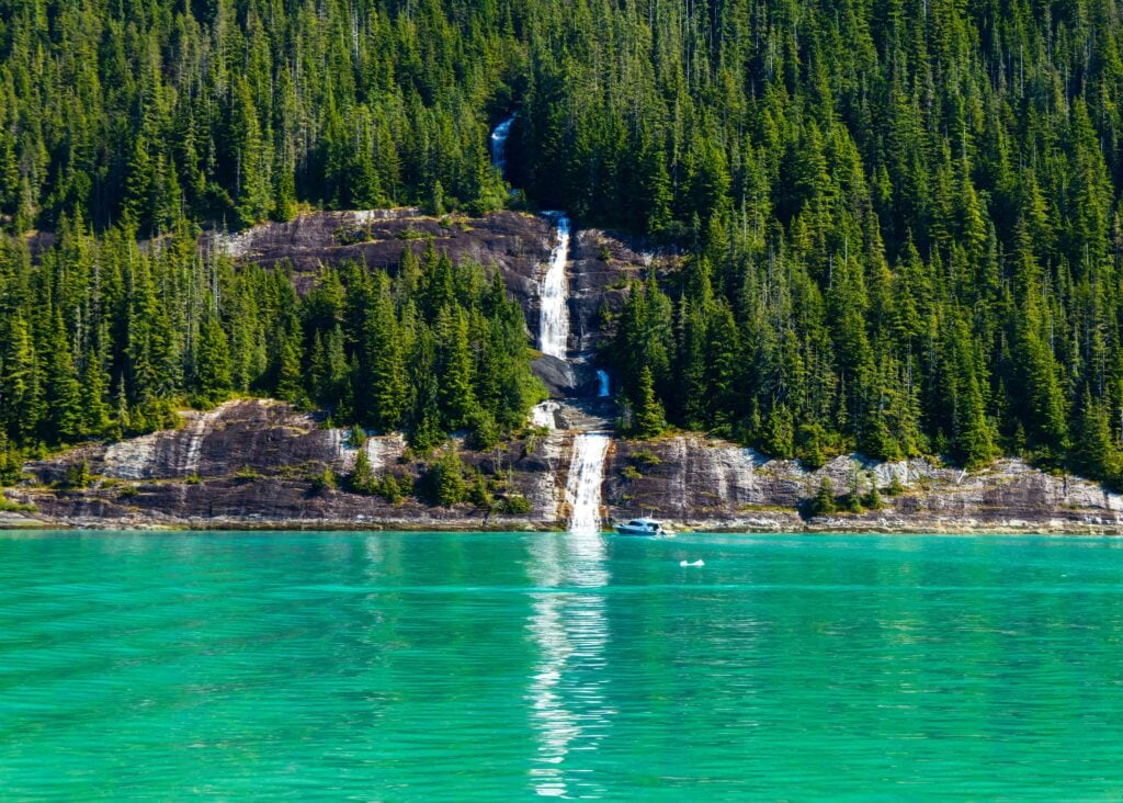 a waterfall flowing into the ocean with a small boat nearby