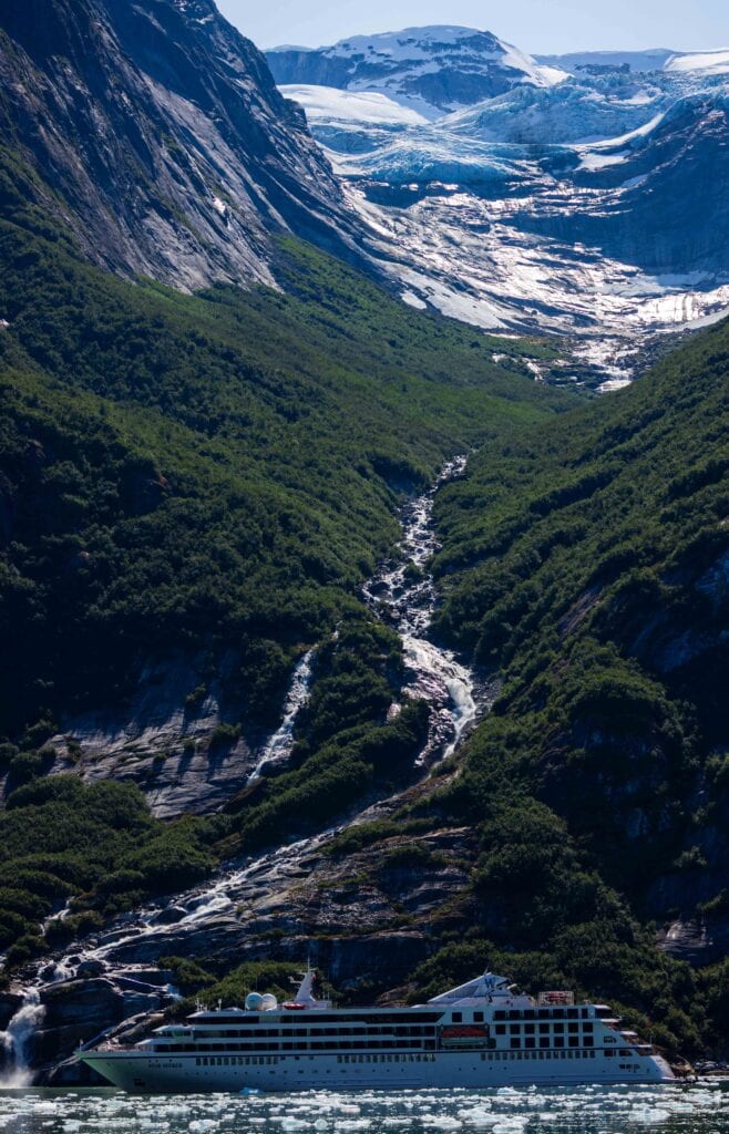 a big waterfall with a cruise ship beneath it on the endicott arm and dawes glacier tour