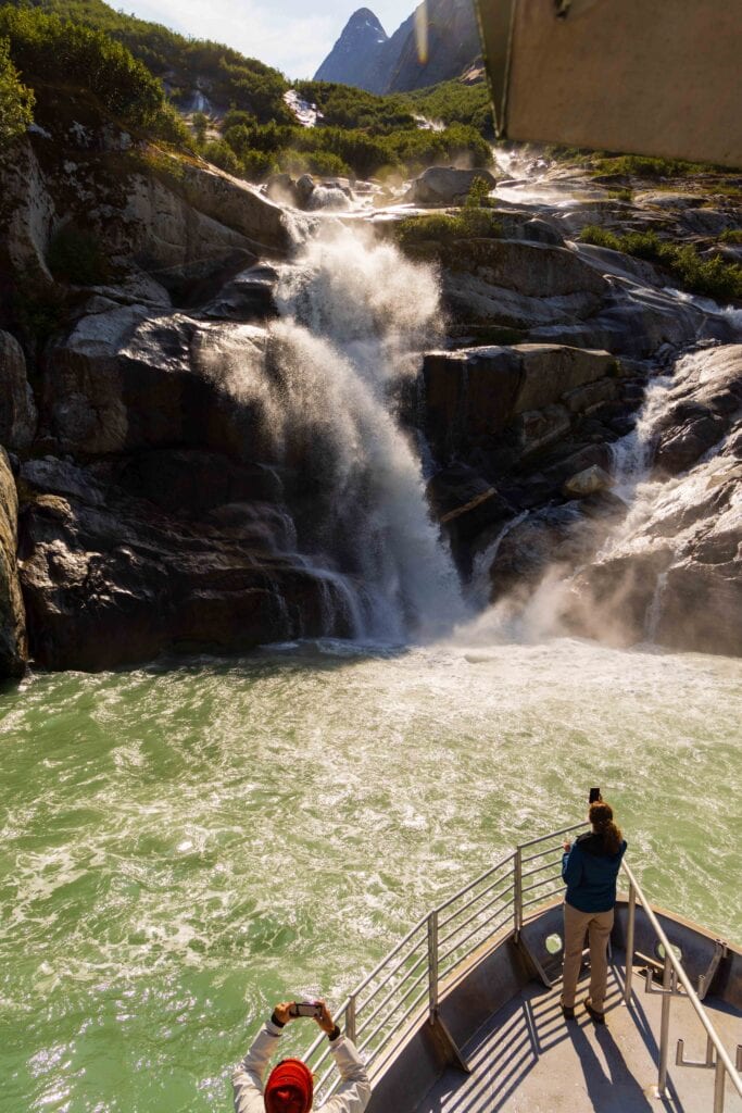 a boat nearing a waterfall that empties into the fjord