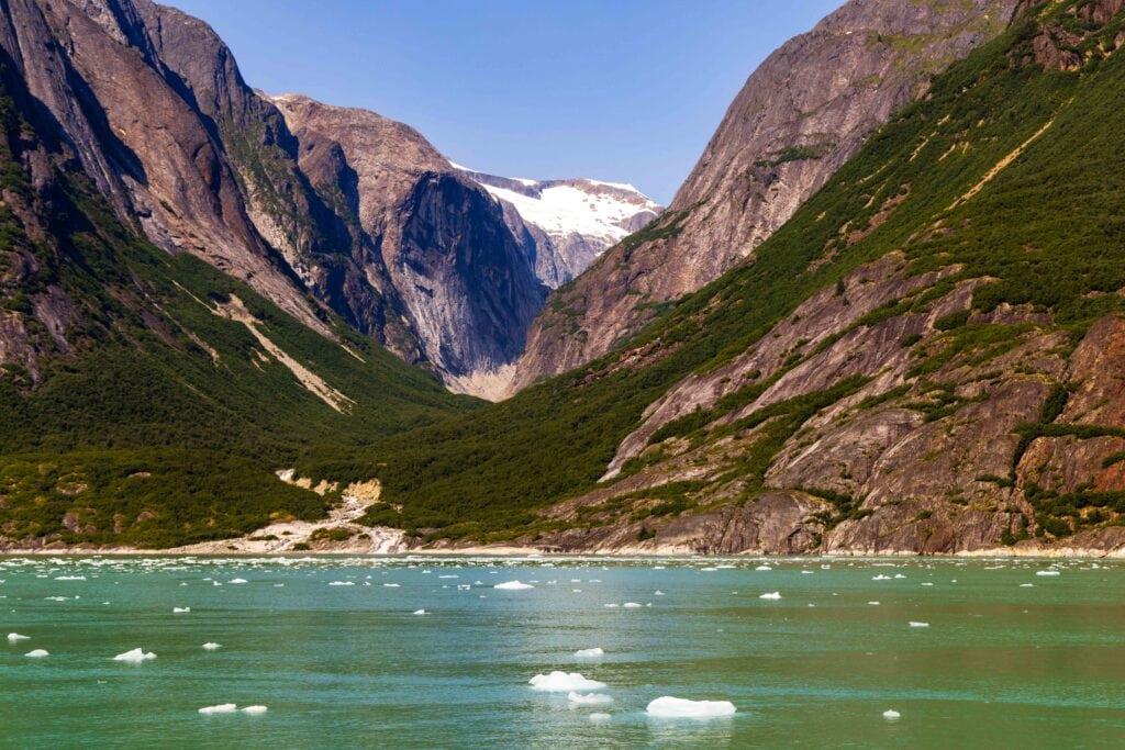 small icebergs float in the fjord with tall mountains around