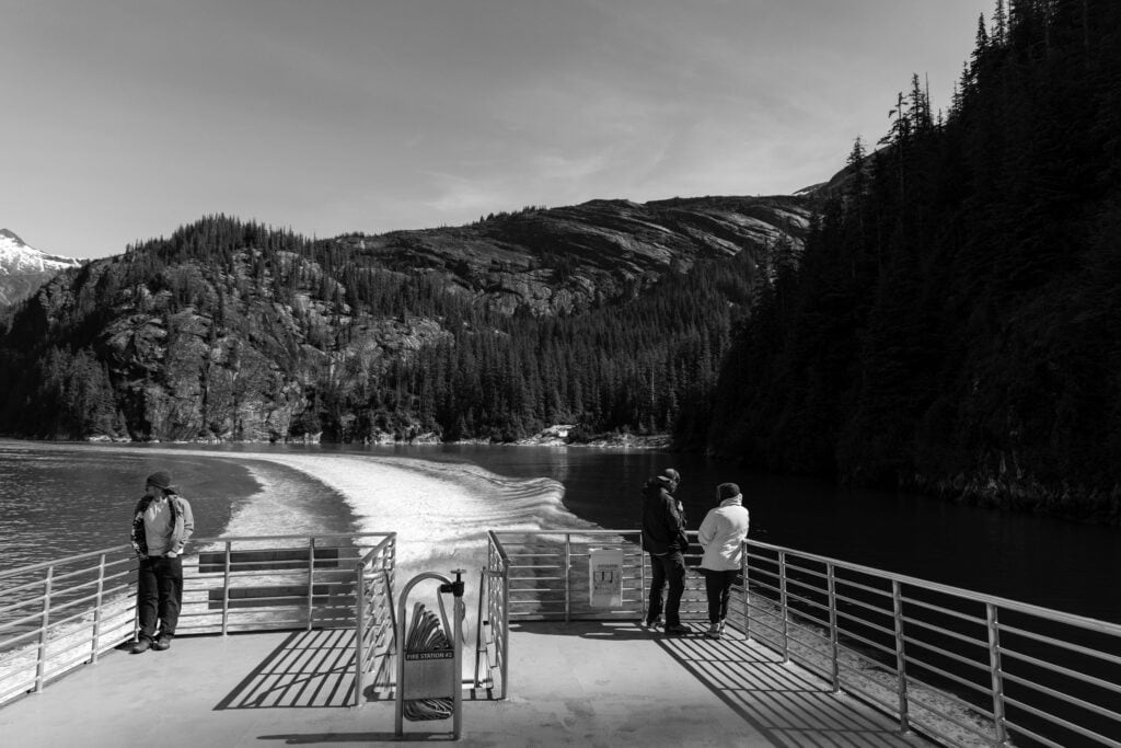 black and white image of people on the back of a tour boat looking at the fjords