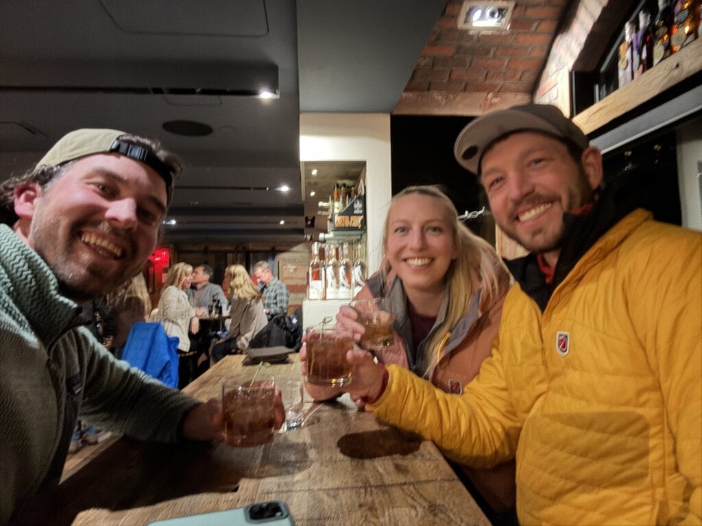 three people smile at the camera holding cocktail glasses