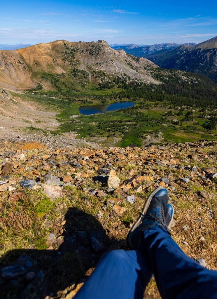 a hikers feet and legs with a lake far below