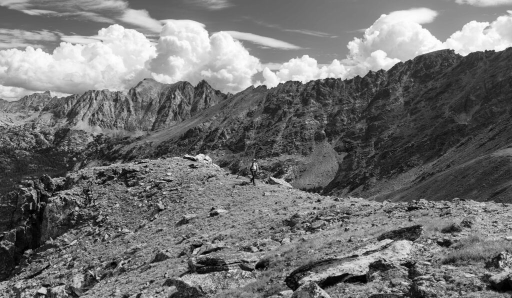 black and white image of a hiker walking on a ridgeline with clouds and mountains above