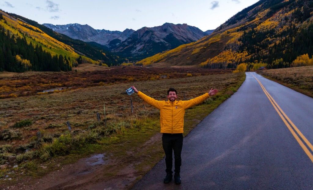 a man holds out his arms near a road in the mountains