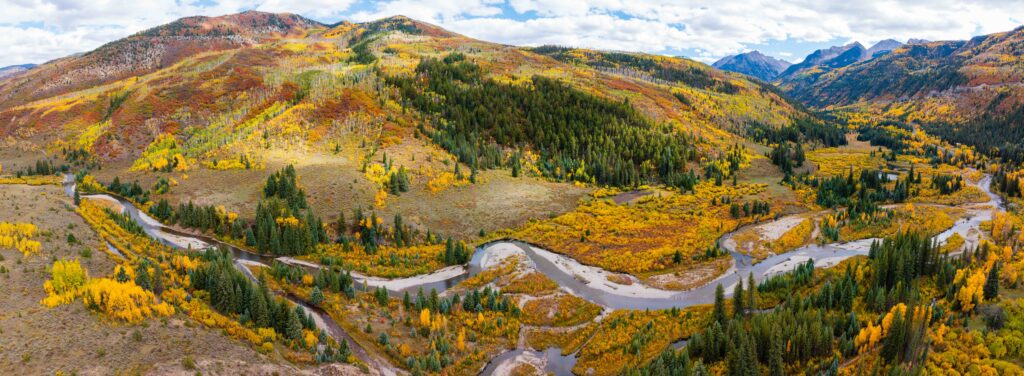 fall colors lining the slopes with a creek and mountains in view