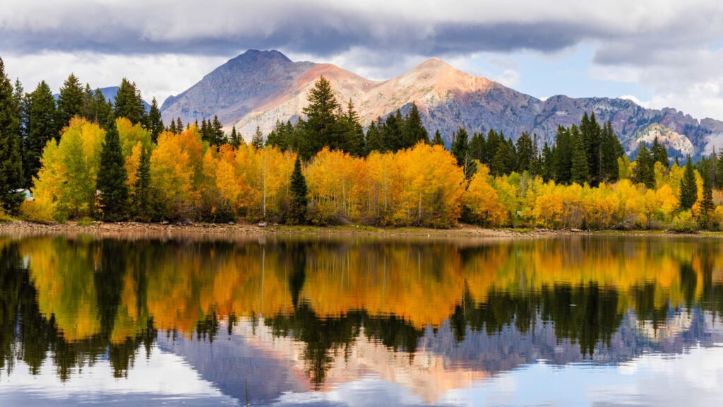 a mountain and clouds with a lake and trees below