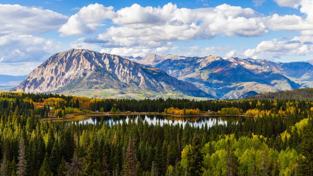 a mountain and clouds with a lake and trees below