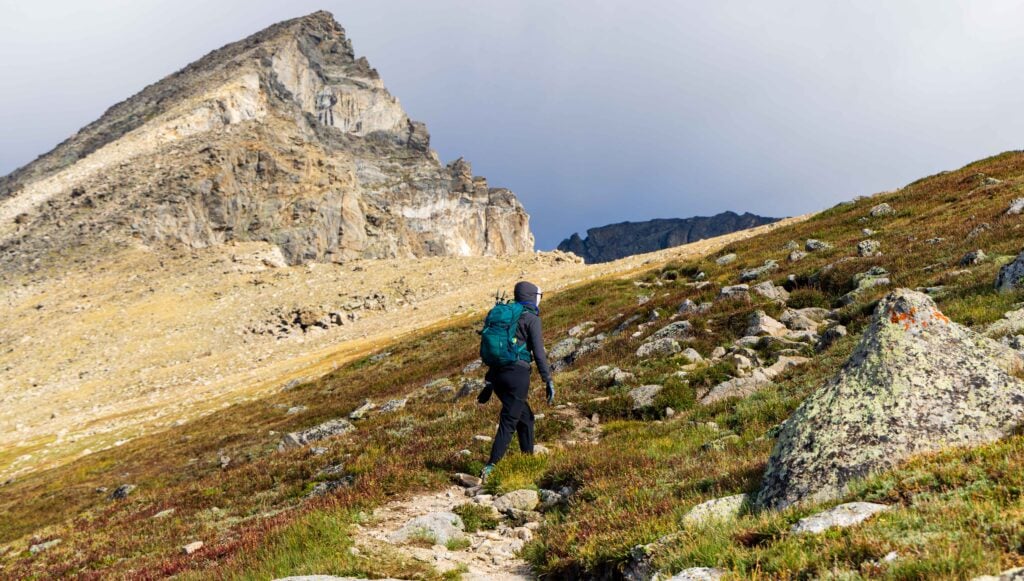 a hiker stands on the trail with a jagged peak above