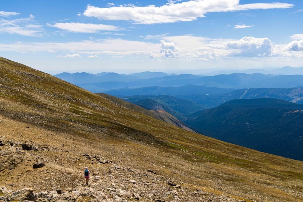a hiker on the trail in the alpine with mountain layers in the distance