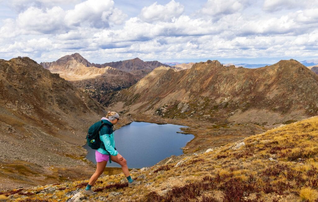 Hiker descending a steep alpine slope above a mountain lake