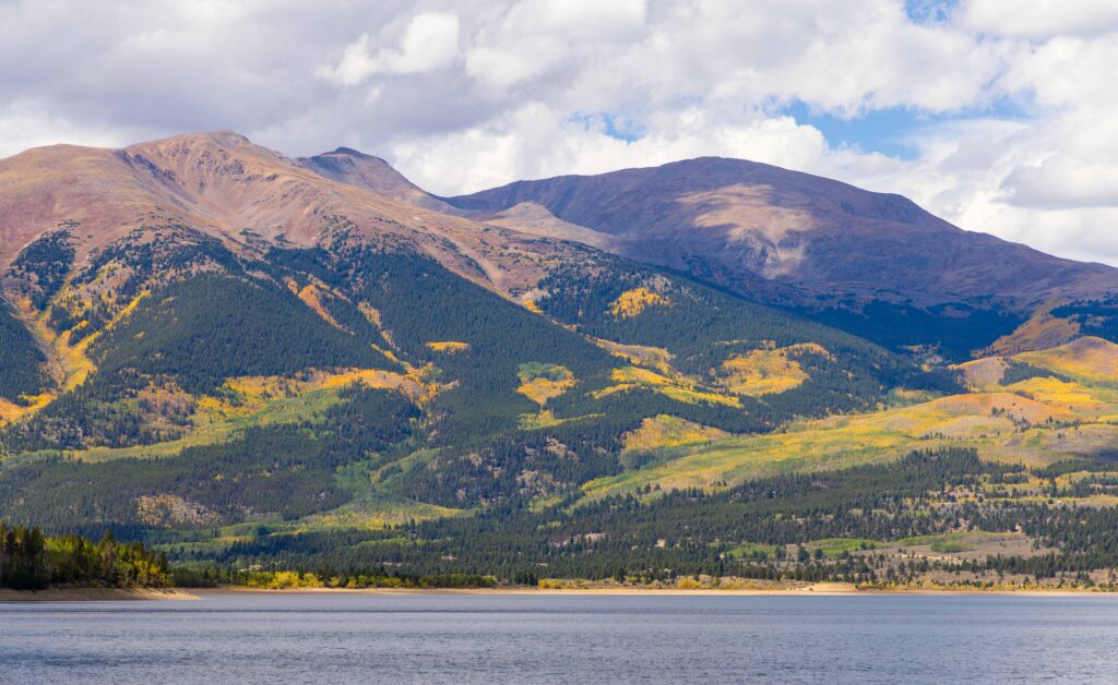 Twin Lakes Reservoir shoreline framed by forested mountain slopes with patches of fall color
