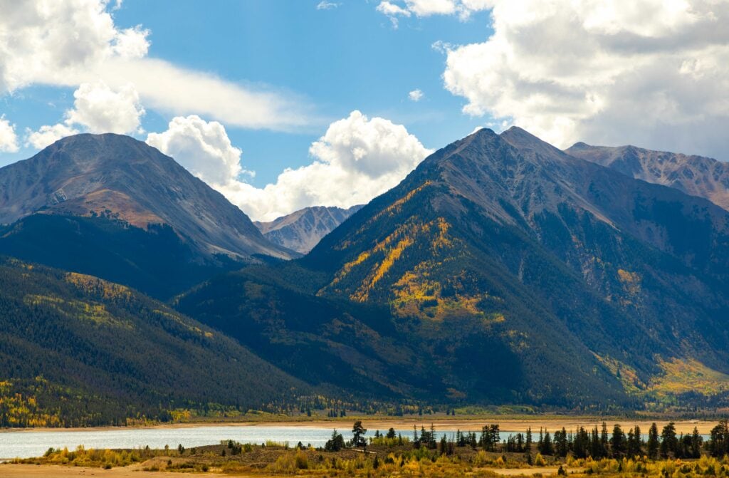 Mountain peaks rising above a lake and forested valley with patches of fall color