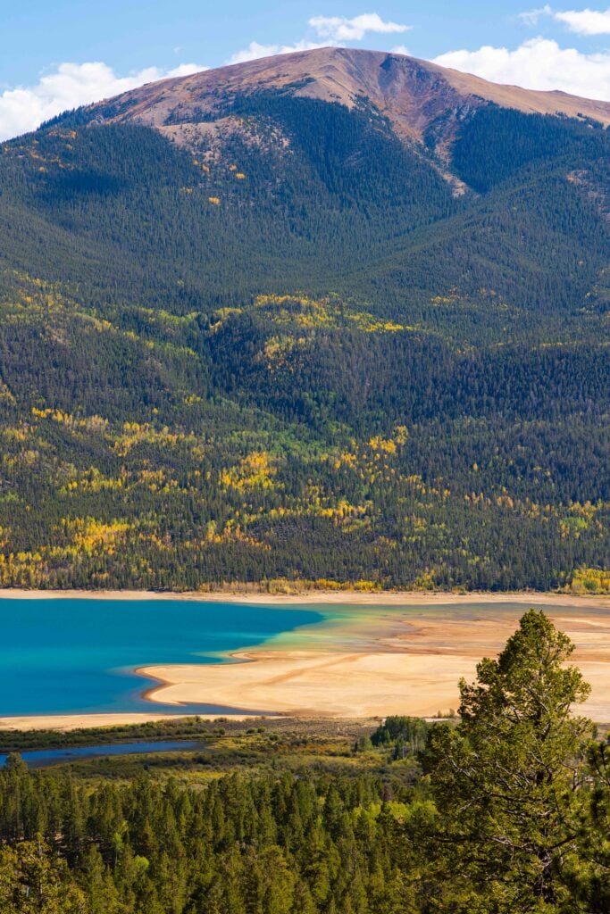 Mountain reservoir with an exposed sandy shoreline below a peak dusted with fall color