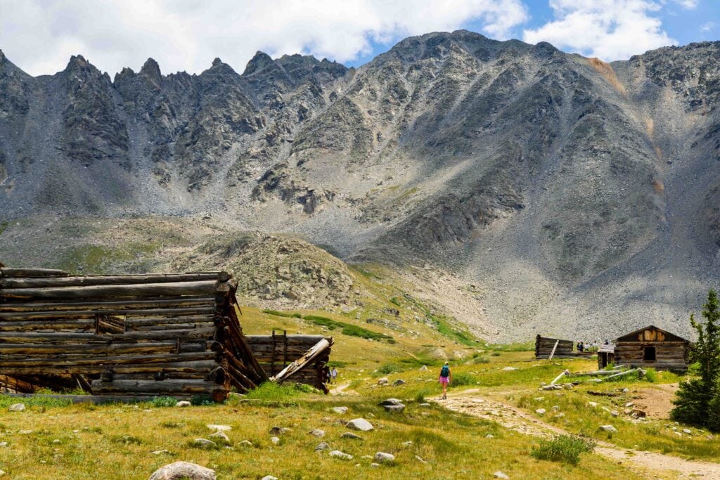 a hiker walk next to an old wooden cabin in the mountains