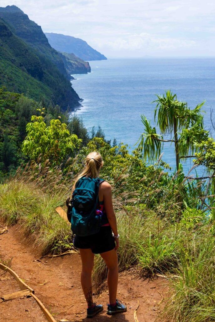a woman looks out from a viewpoint high above the pacific ocean along the na pali coast on the hanakapiai beach hike