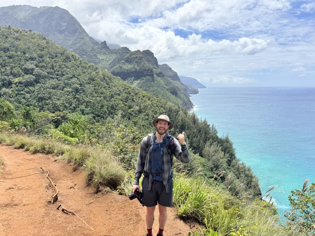 the author smiles with a view of the na pali coast behind him on the a couple pose for a photo along the Kalalau Trail to Hanakapi'ai Beach