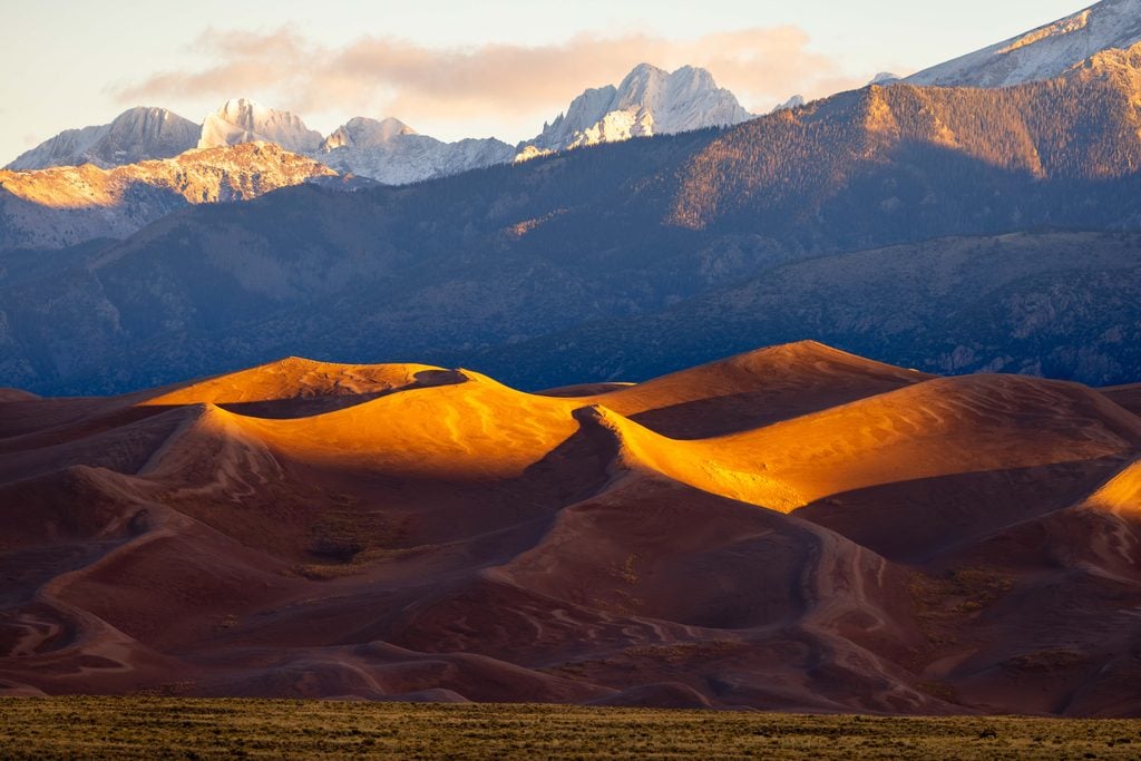the great sand dunes at sunrise with snow capped peaks above it