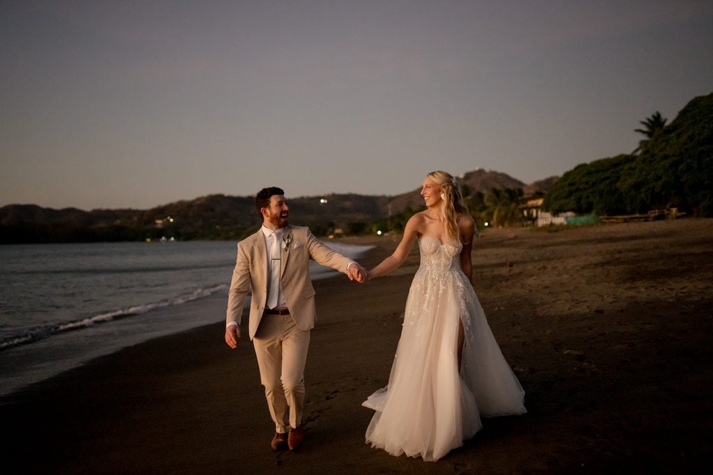 a man and woman walk on the beach in costa rica in their wedding attire